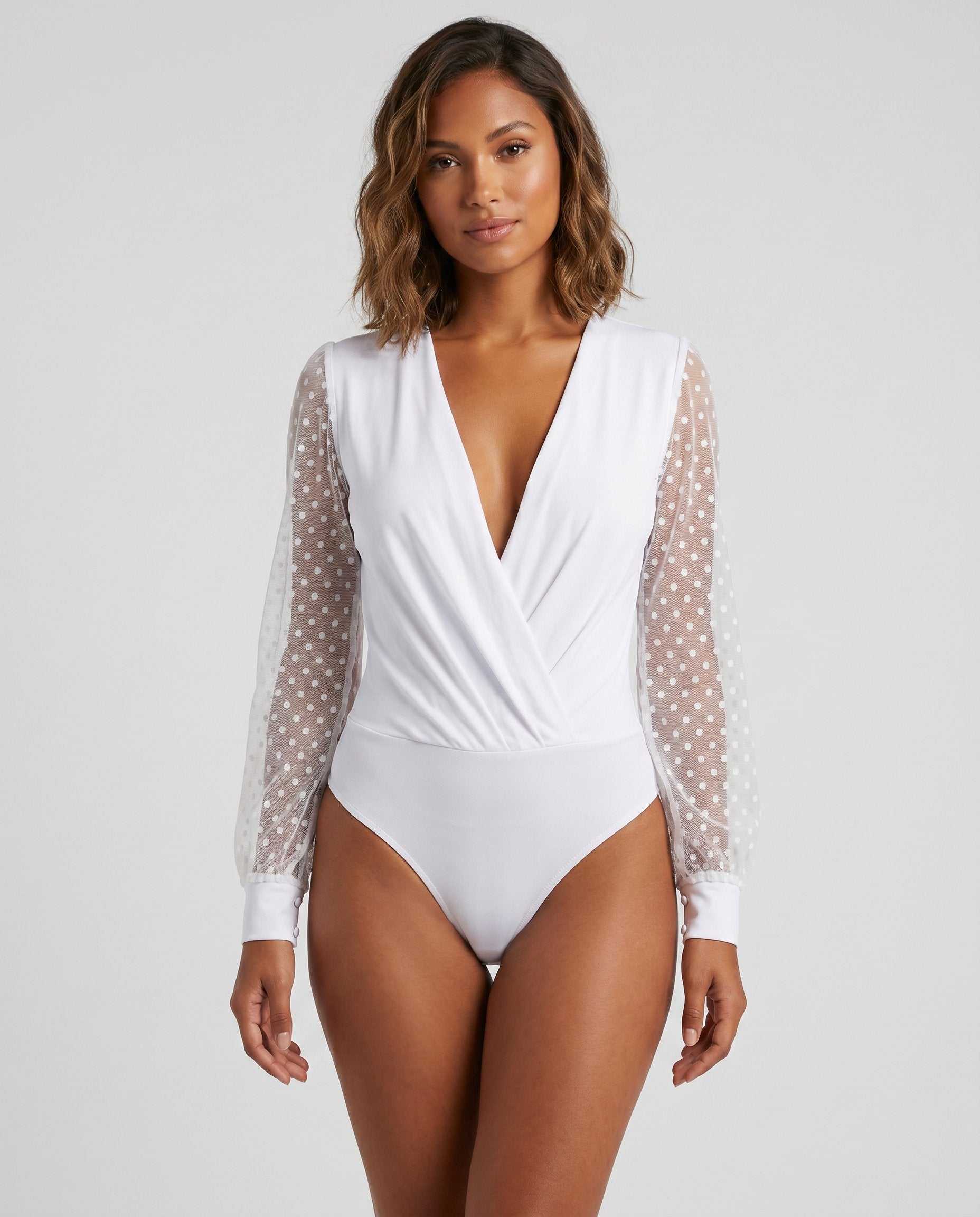 White polka dot mesh plunge wrap bodysuit by ROMAR, featuring a fitted design with long sleeves and a deep V neckline.